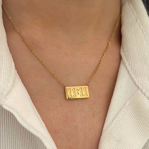 Gold necklace with '11:11' pendant worn by a person in a white shirt.