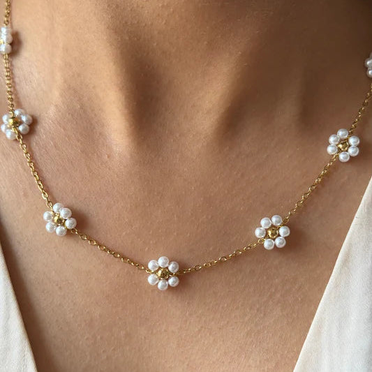 Gold necklace with pearl flower pendants on a person wearing a white top.