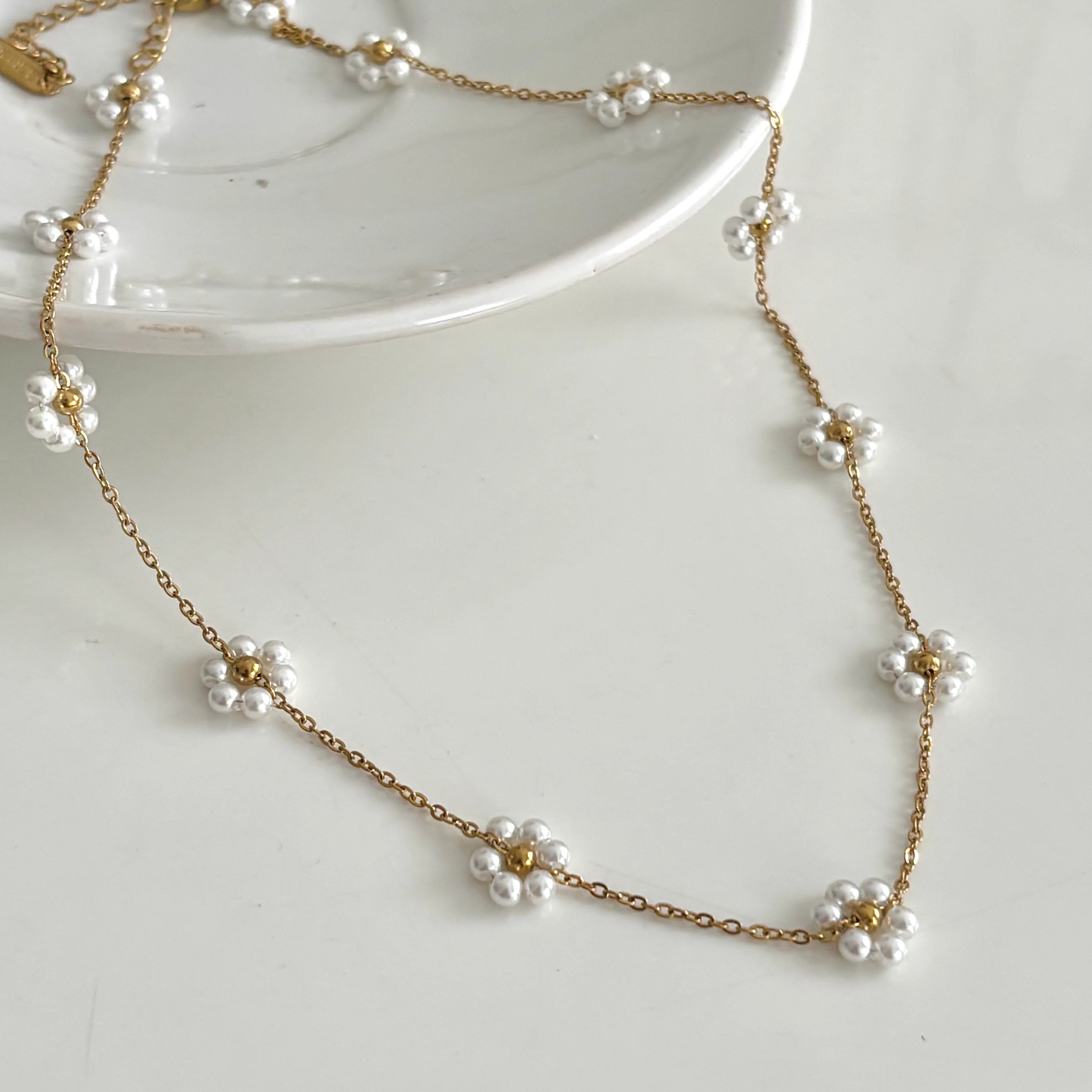 Gold necklace with white floral pendants on a white surface