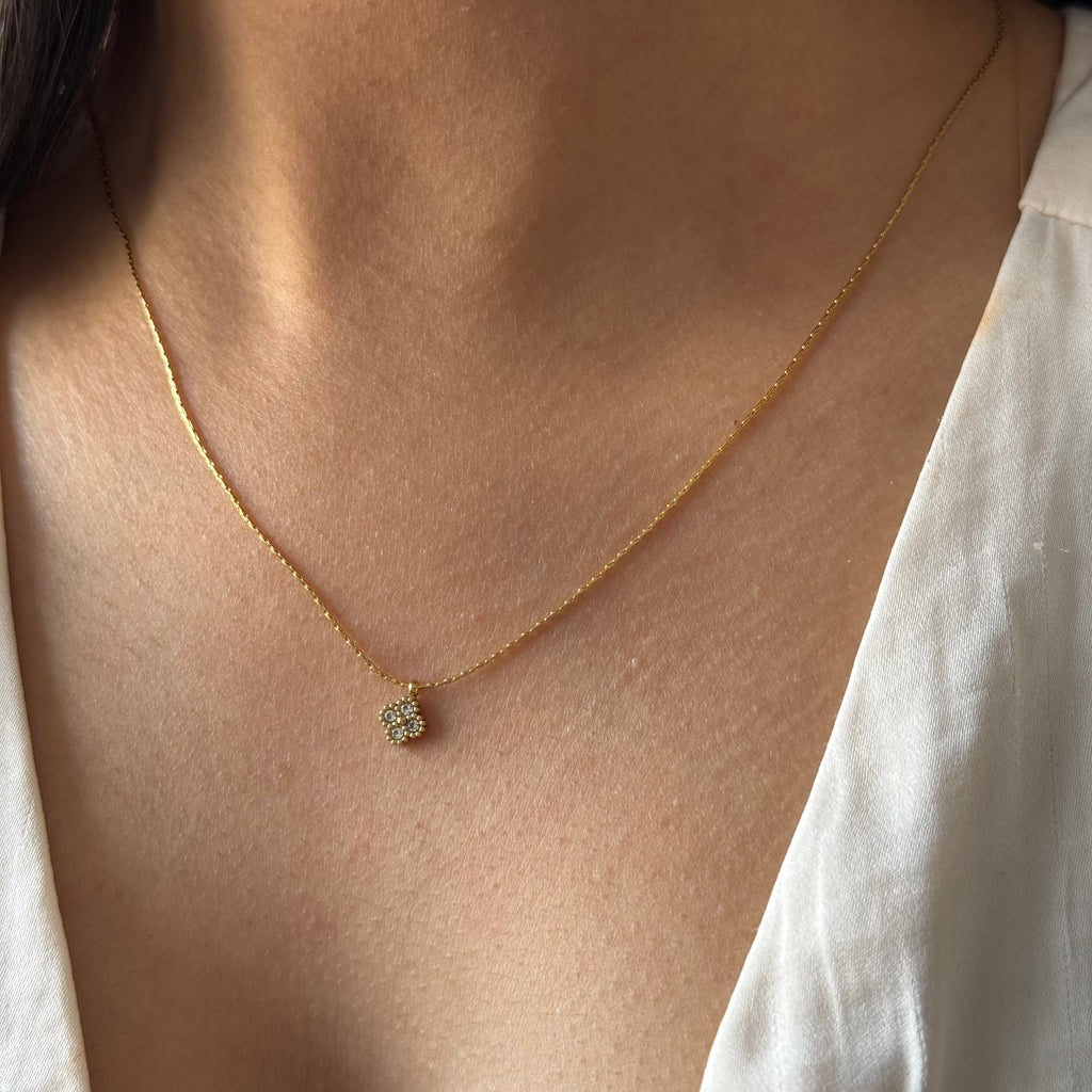 Gold necklace with a small pendant on a person wearing a white shirt.