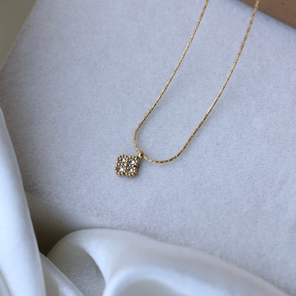 Gold necklace with a square pendant on a light gray surface