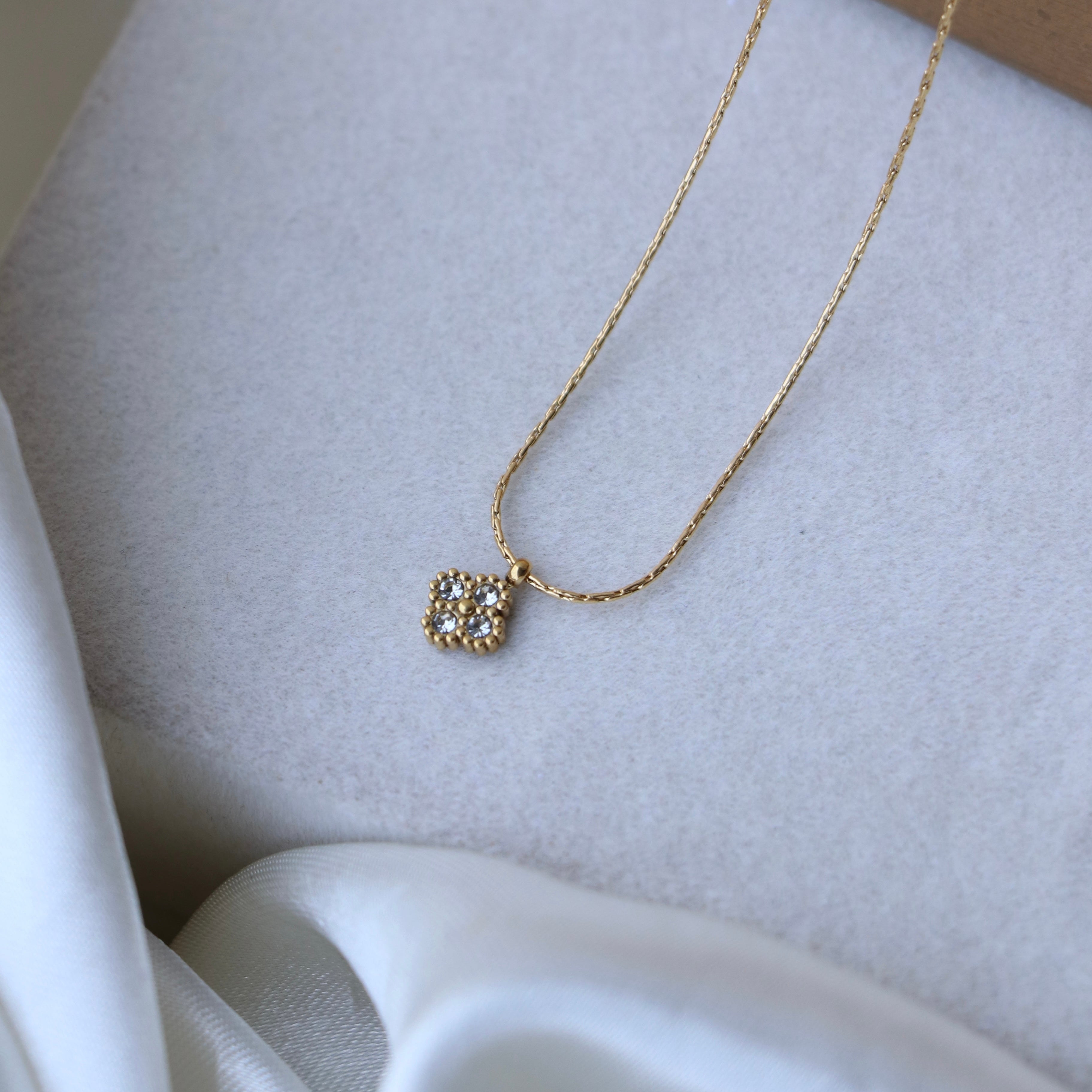 Gold necklace with a square pendant on a light gray surface
