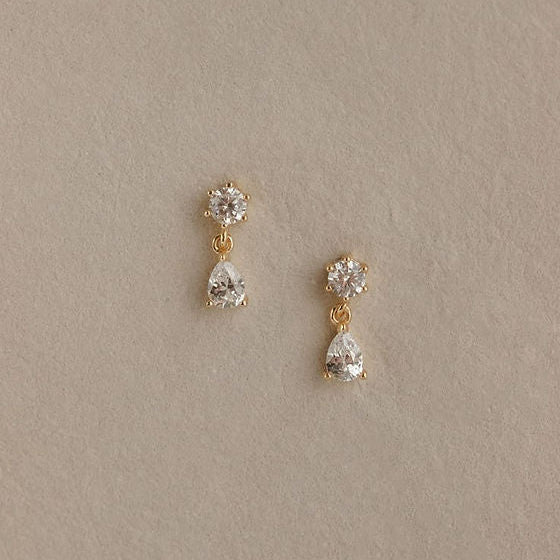 Pair of gold and crystal drop earrings on a beige background