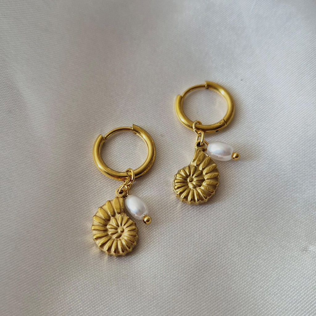 Gold hoop earrings with floral designs and pearls on a light gray background